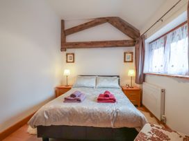A bedroom with a double bed two bedside tables and lamps wooden beams on the wall and window with curtains at Oak Cottage in Aylesbeare