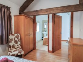 A bedroom with wooden wardrobe floral chair dresser and bathroom visible at Oak Cottage in Aylesbeare