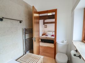 A bathroom with a toilet, towel rack, and a doorway leading to a bedroom with a bed and wooden beams at Oak Cottage in Aylesbeare