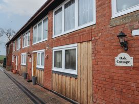 A brick and wood exterior of a cottage with multiple windows potted plants and lamps at Oak Cottage in Aylesbeare