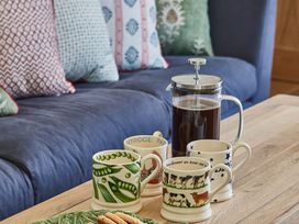 A wooden table with four decorated mugs a French press with coffee and a plate of cookies in front of a blue sofa with patterned cushions at The Stables at Galteemore Farm in Avebury near Marlborough