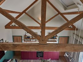 A kitchen with wooden beams overhead and purple cabinets with shelves above at The Stables in Galteemore Farm in Avebury near Marlborough