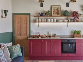 A kitchen with red cabinets wooden shelves with cups and plates plants and a wooden door at The Stables in Galteemore Farm in Avebury near Marlborough