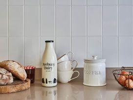 A kitchen countertop with bread on a wooden cutting board a jar of jam a bottle of milk stacked cups a coffee canister and a wire basket of eggs at The Stables in Galteemore Farm in Avebury near Marlborough
