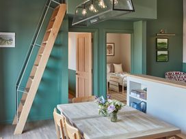 A dining area with a wooden table, chairs, a wooden ladder, green walls, and a view of a bedroom at The Stables in Galteemore Farm in Avebury near Marlborough
