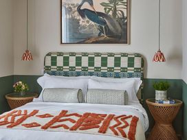 A bedroom with a bed with patterned headboard and orange decorative blanket with side tables and hanging lamps at The Stables in Galteemore Farm in Avebury near Marlborough