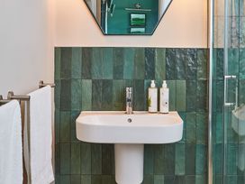 A bathroom sink with soap dispensers towels on a rack and green tiled walls at The Stables in Galteemore Farm in Avebury near Marlborough