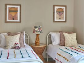 A bedroom with two single beds a lamp on a wicker side table and framed hot air balloon prints on the wall at The Stables Galteemore Farm in Avebury near Marlborough