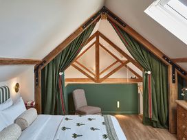A bedroom with a bed and patterned bedding a chair green curtains and wooden beams at The Stables in Galteemore Farm in Avebury near Marlborough