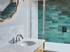 A bathroom with a white sink and silver faucet next to a bathtub with green tiled wall at The Stables in Galteemore Farm in Avebury near Marlborough