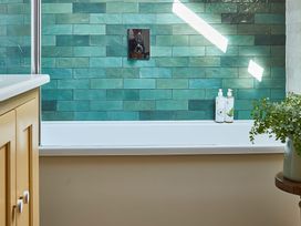A bathroom with a bathtub beside a wooden cabinet and a potted plant at The Stables in Galteemore Farm in Avebury near Marlborough