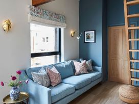 A living room with a blue sofa and patterned pillows next to a window with a floral vase on a side table at The Stables in Galteemore Farm in Avebury near Marlborough