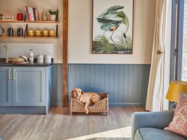 A kitchen area with blue cabinets yellow cups bread on the counter and a dog in a wicker basket at The Stables in Galteemore Farm in Avebury near Marlborough