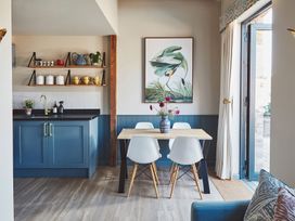 A dining area with a wooden table and four white chairs next to a blue kitchen cabinet and open shelves at The Stables in Galteemore Farm in Avebury near Marlborough