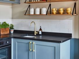 A kitchen corner with blue cabinets black countertop brass faucet white tiled backsplash wooden shelves with canisters and yellow cups at The Stables in Galteemore Farm in Avebury near Marlborough
