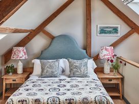 A bedroom with a bed featuring a blue headboard two patterned pillows bedside tables with lamps and flowers under exposed wooden beams at The Stables Galteemore Farm in Avebury near Marlborough