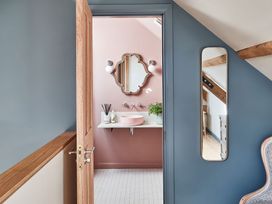 A bathroom with a pink wall a pink sink a mirror and two lights seen through an open wooden door from a blue wall hallway