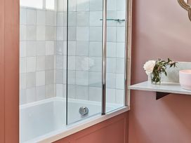 A bathroom with a bathtub tiled walls glass shower screen and a shelf with a flower vase at The Stables Galteemore Farm in Avebury near Marlborough