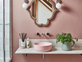 A bathroom sink area with a pink basin a decorative mirror and two wall lights at The Stables Galteemore Farm in Avebury near Marlborough
