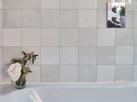 A bathroom wall with square tiles a flower vase with pink roses and a metal control panel at The Stables in Galteemore Farm in Avebury near Marlborough