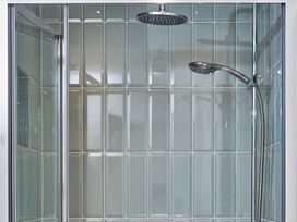 A shower area with glass tiled walls and two shower heads at The Stables Galteemore Farm in Avebury near Marlborough