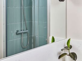 A bathroom shower with green tiles a chrome showerhead and a plant in a white pot at The Stables in Galteemore Farm in Avebury near Marlborough