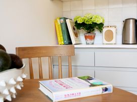 A kitchen corner with a wooden chair a book on a table a bowl of avocados cookbooks a potted plant a speaker and a kettle on a kitchen counter at The Stables Galteemore Farm in Avebury near Marlborough