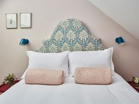 A bed with patterned headboard white pillows and two cylindrical cushions with side tables and lamps at The Stables in Galteemore Farm in Avebury near Marlborough