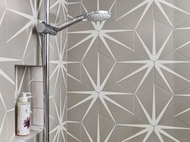 A shower area with a chrome showerhead and a bottle on a built-in shelf with geometric patterned tiles at The Stables Galteemore Farm in Avebury near Marlborough
