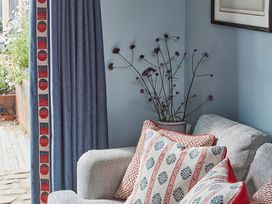 A corner of a room with a grey patterned sofa cushions with red and blue designs a vase with tall purple flowers and blue curtains at The Stables at Galteemore Farm in Avebury near Marlborough