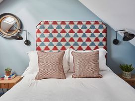 A bed with patterned headboard and two decorative pillows two bedside tables with plants and books and wall lamps at The Stables Galteemore Farm in Avebury near Marlborough