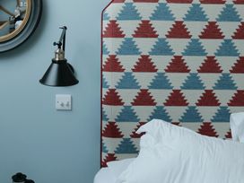 A patterned fabric headboard with red and blue geometric shapes beside a wall with a black wall lamp and a white switch at The Stables in Galteemore Farm in Avebury near Marlborough