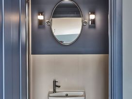 A bathroom sink with a faucet below an oval mirror and two wall lights at The Stables in Galteemore Farm in Avebury near Marlborough