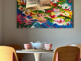 A dining area with a round white table wooden chairs a white teapot two cups on a tray and a colorful abstract painting on the wall at The Stables in Galteemore Farm in Avebury near Marlborough