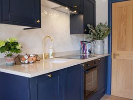 A kitchen with dark blue cabinets a beige countertop an oven and a sink with a gold faucet at The Stables Galteemore Farm in Avebury near Marlborough
