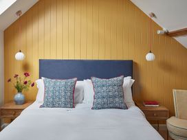 A bedroom with a blue headboard white bedding patterned pillows wooden bedside tables hanging white pendant lights and a vase with flowers at The Stables in Galteemore Farm in Avebury near Marlborough