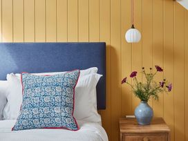 A bed with white pillows and a blue patterned cushion next to a wooden nightstand with a vase of flowers and a hanging white light at The Stables in Galteemore Farm in Avebury near Marlborough