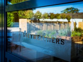 A glass door with the word GREWEATHERS printed on it and garden visible through the glass at The Stables in Galteemore Farm in Avebury near Marlborough