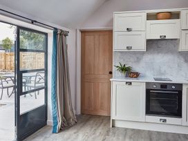 A kitchen area with white cabinets a built-in oven a wooden door and a glass door leading outside at The Stables Galteemore Farm in Avebury near Marlborough