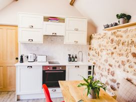 A kitchen with white cabinets, an oven, a wooden table with a plant, and a stone wall at The Stables in Galteemore Farm in Avebury near Marlborough
