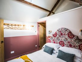 A bedroom with a bed with patterned headboard and pillows a wooden door and wall-mounted coat rack at The Stables in Galteemore Farm in Avebury near Marlborough