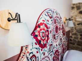Wall-mounted lamps on each side of a bed with a patterned headboard and a stone wall at The Stables in Galteemore Farm in Avebury near Marlborough