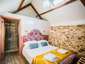 A bedroom with a bed with colorful headboard and folded towels on a blanket next to a stone wall at The Stables at Galteemore Farm in Avebury near Marlborough