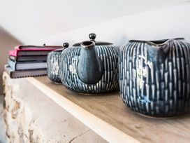A wooden shelf with a patterned teapot, a matching creamer, and stacked books at The Stables in Galteemore Farm in Avebury near Marlborough