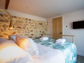 A bedroom with a bed folded towels a stone wall a wooden door and a mounted TV at The Stables in Galteemore Farm in Avebury near Marlborough