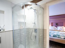 A bathroom with a corner glass shower enclosure and a bedroom visible through the door at The Stables Galteemore Farm in Avebury near Marlborough