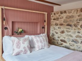 A bed with patterned pillows against a pink paneled wall and a stone wall at The Stables in Galteemore Farm in Avebury near Marlborough