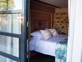 A bedroom with a bed pillows bedside lamps and a stone wall visible through a partially open door at The Stables in Galteemore Farm in Avebury near Marlborough