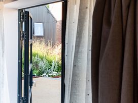 An open door showing a garden with flowering plants and a small building with black siding at The Stables in Galteemore Farm in Avebury near Marlborough
