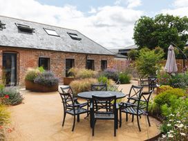 An outdoor patio area with black metal table and six chairs surrounded by flower beds and shrubs at The Stables in Galteemore Farm in Avebury near Marlborough